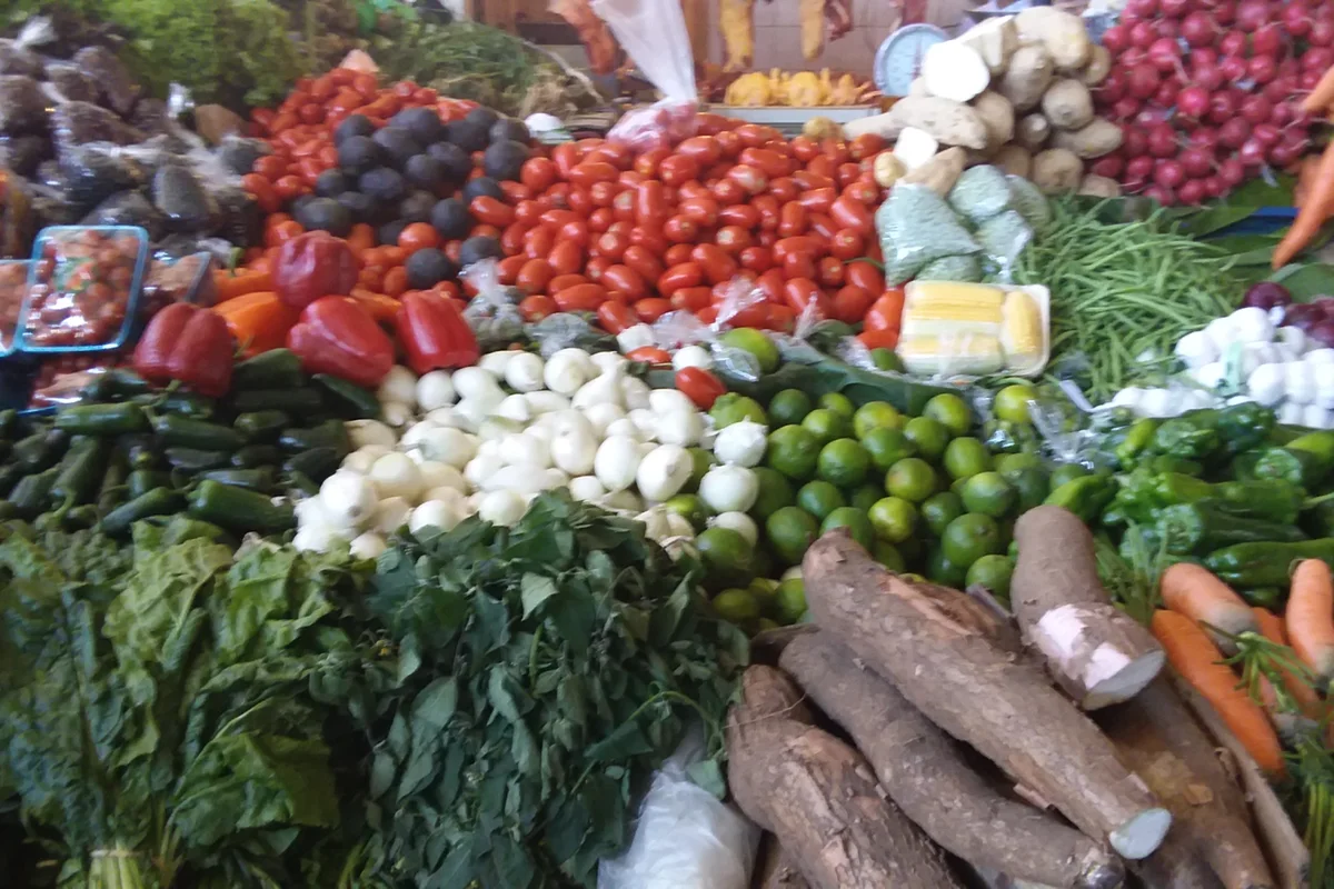 Puesto de verduras en un mercado guatemalteco con tomate, cebolla, güisquil, zanahoria, repollo, hierbas y yuca