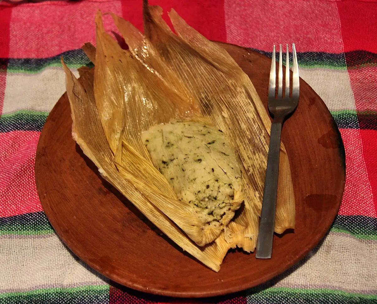 Tamal de chipilín abierto en su hoja, con la masa verde y el relleno a la vista