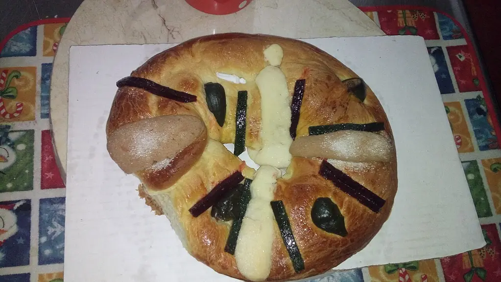 Rosca de reyes de estilo mexicano sobre una mesa, con decoración de frutas