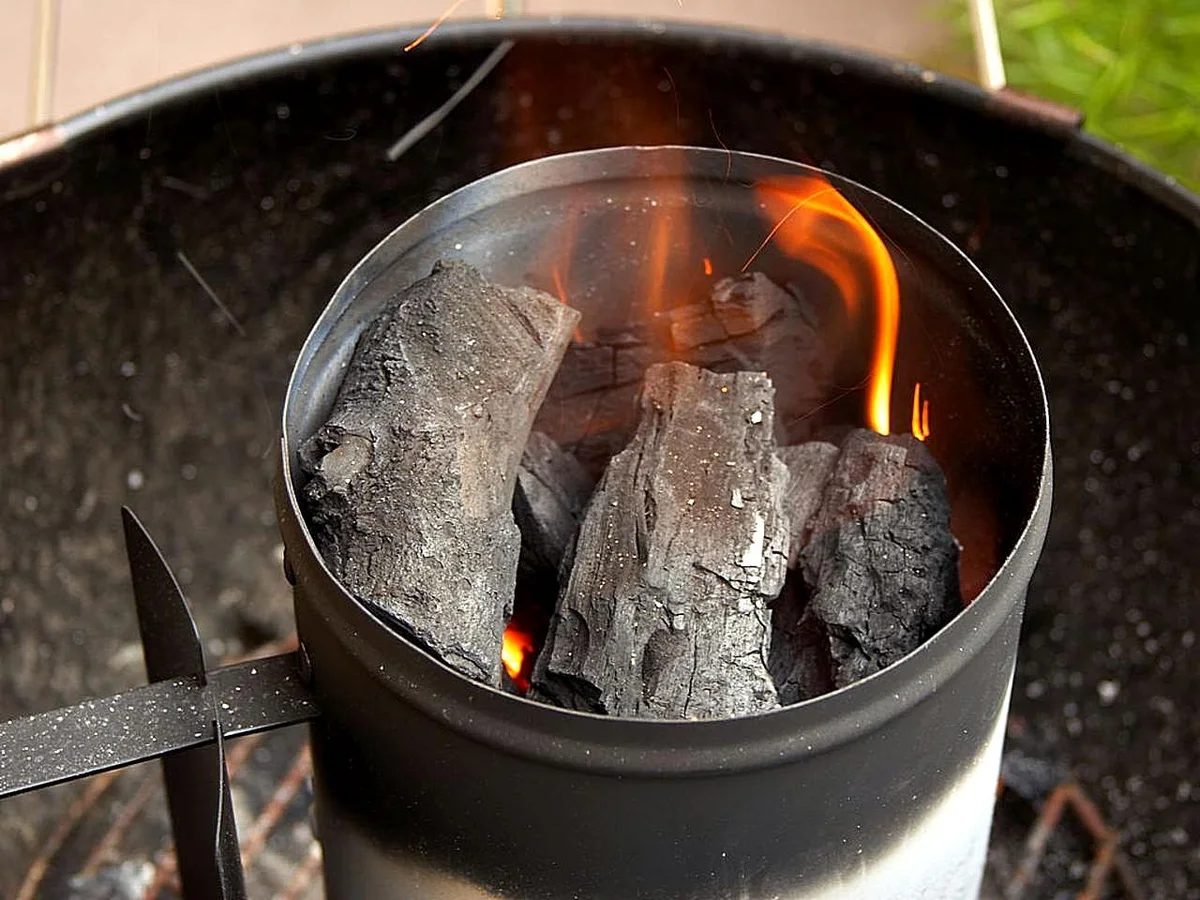 Chimenea de encendido metálica con trozos de carbón encendidos y una llama naranja que sube por dentro