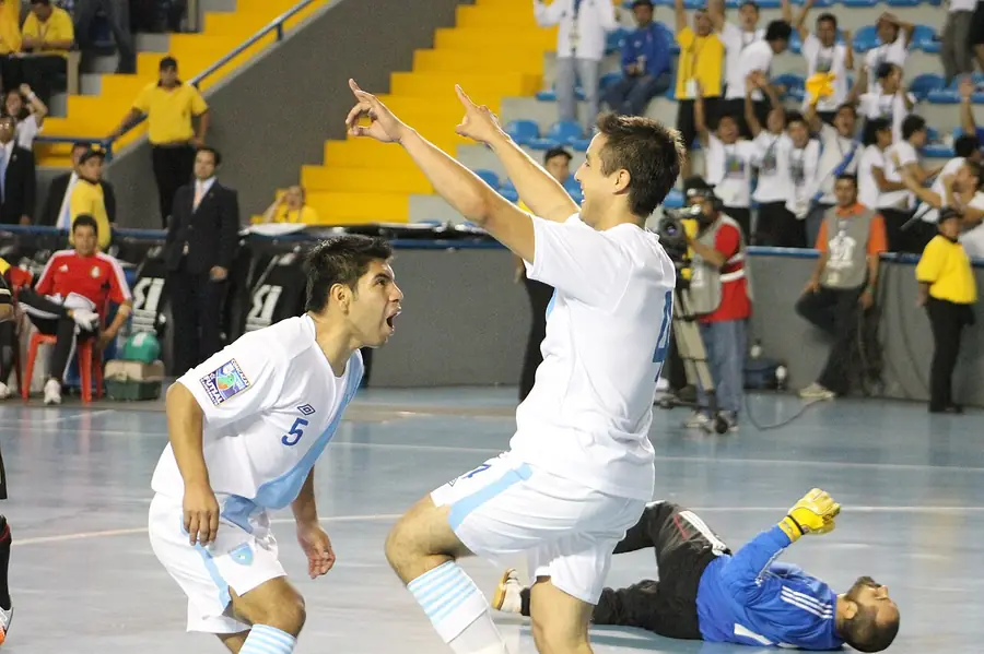 Dos jugadores celebran un gol en un partido de fútbol sala, con camisetas blancas y celestes