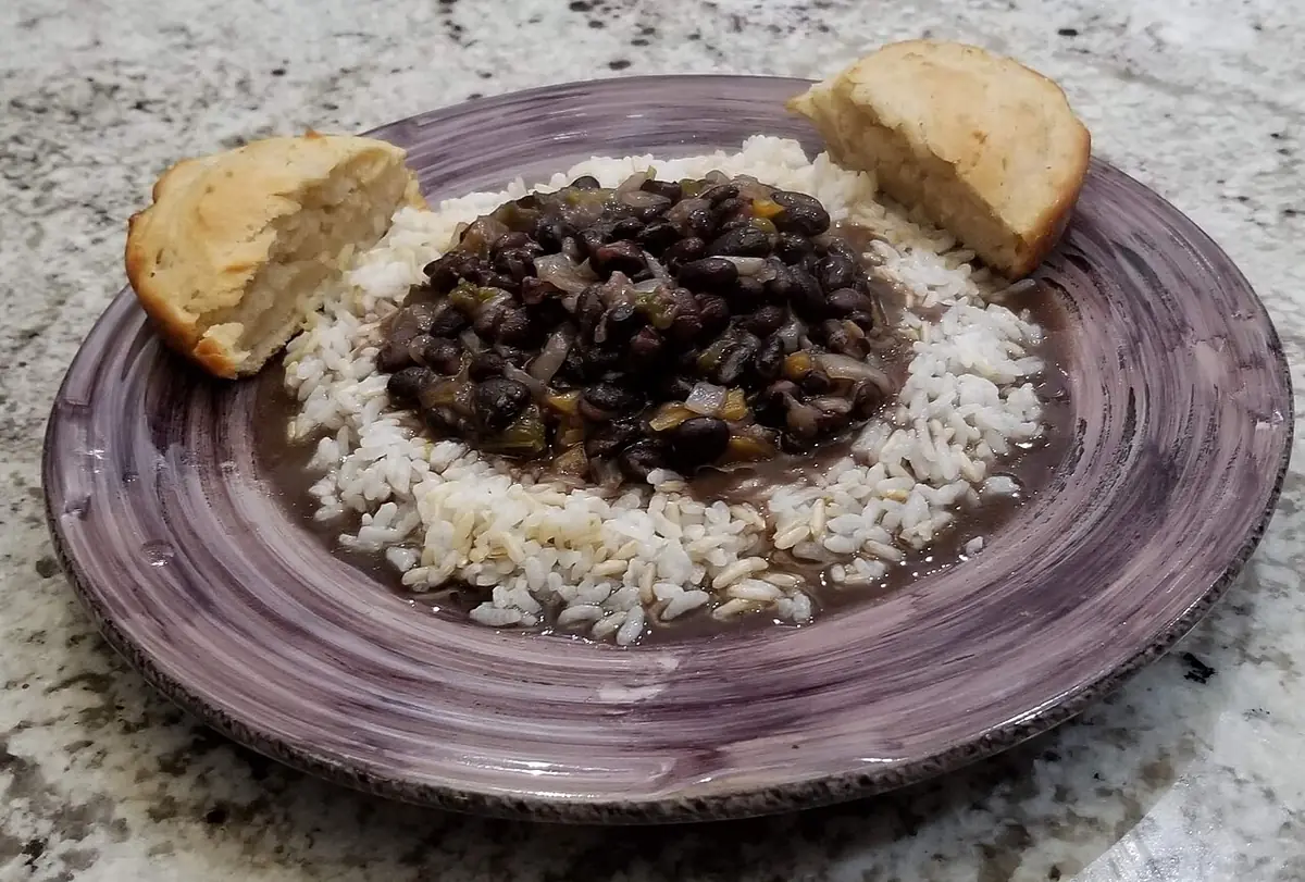 Plato con frijoles negros guisados sobre arroz blanco, con dos trozos de pan