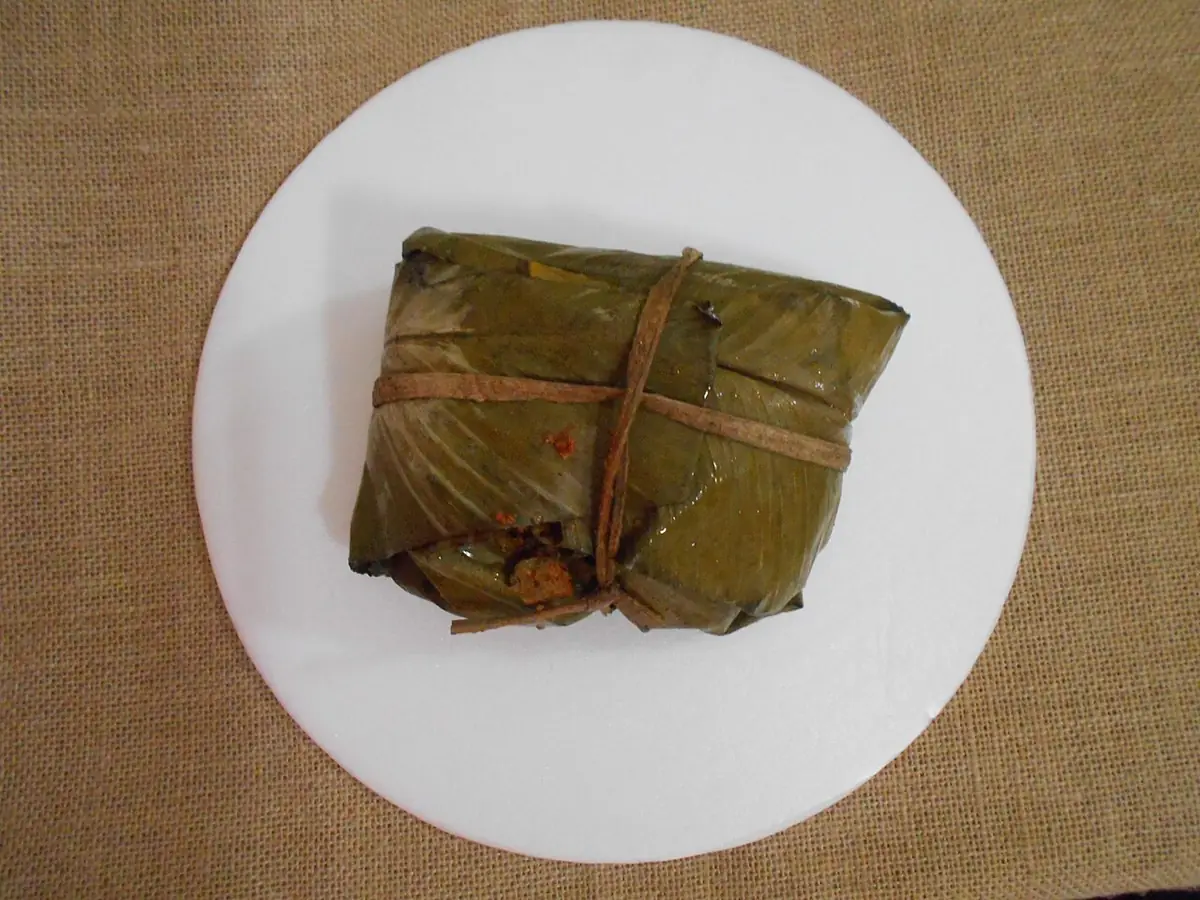 Tamal envuelto en hoja y atado con tiras, servido en un plato blanco