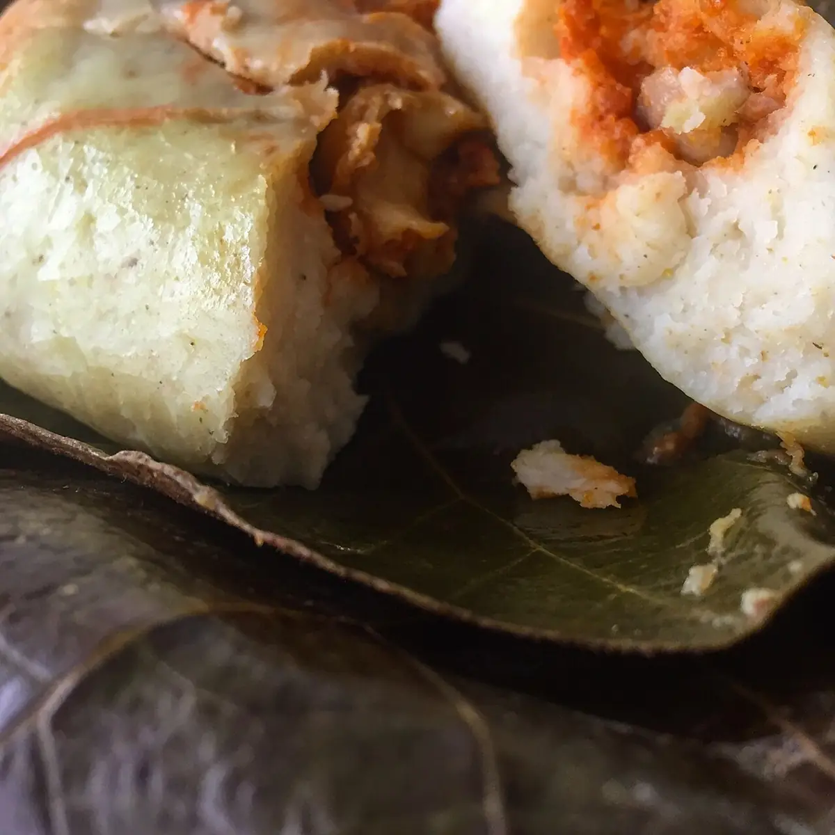 Chuchito partido sobre una hoja, con masa blanca y relleno rojo a la vista