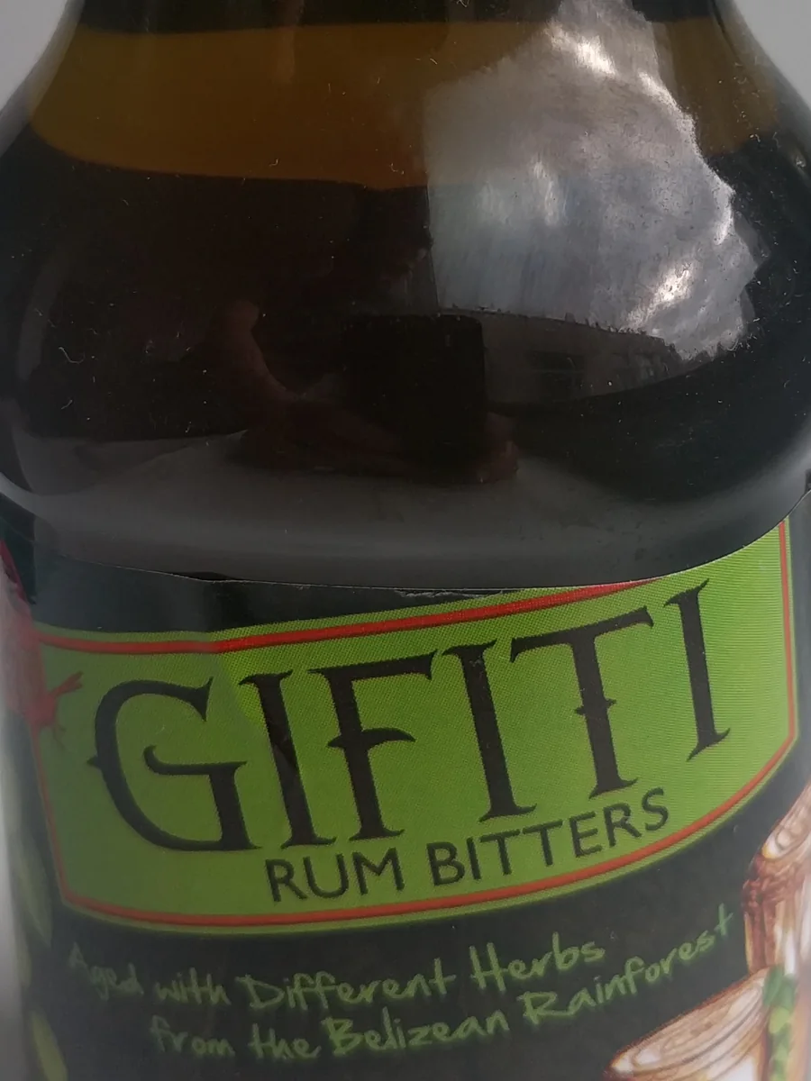 Botella de gifiti de 250 mililitros con licor oscuro y etiqueta verde que dice Gifiti Rum Bitters y aclara que envejeció con hierbas distintas