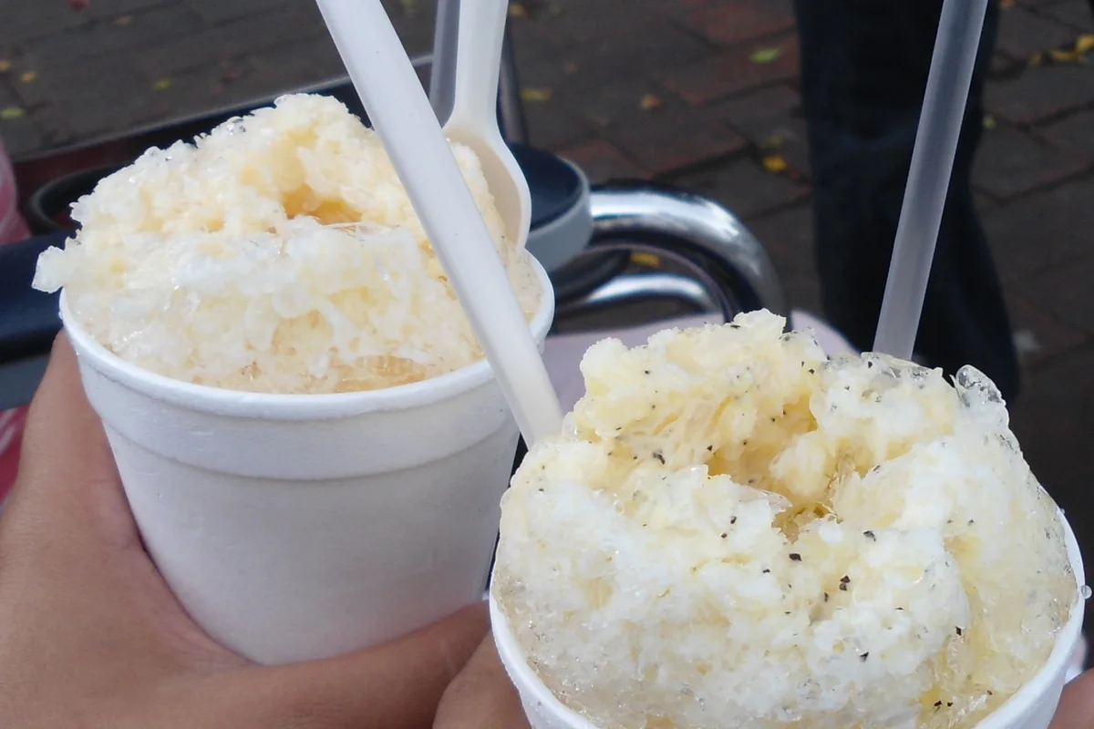 Dos vasos de granizada con hielo raspado, bañados con jarabe de maracuyá y leche condensada, sostenidos en la calle