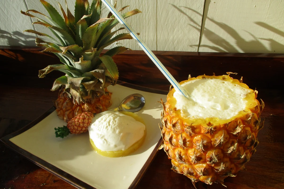 Piña colada servida dentro de una piña abierta, con una bola de helado sobre una rodaja de piña y una cuchara en el plato