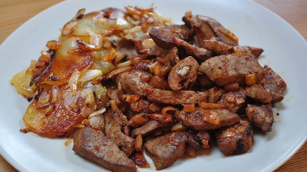 Hígado encebollado servido con cebolla caramelizada y papas doradas