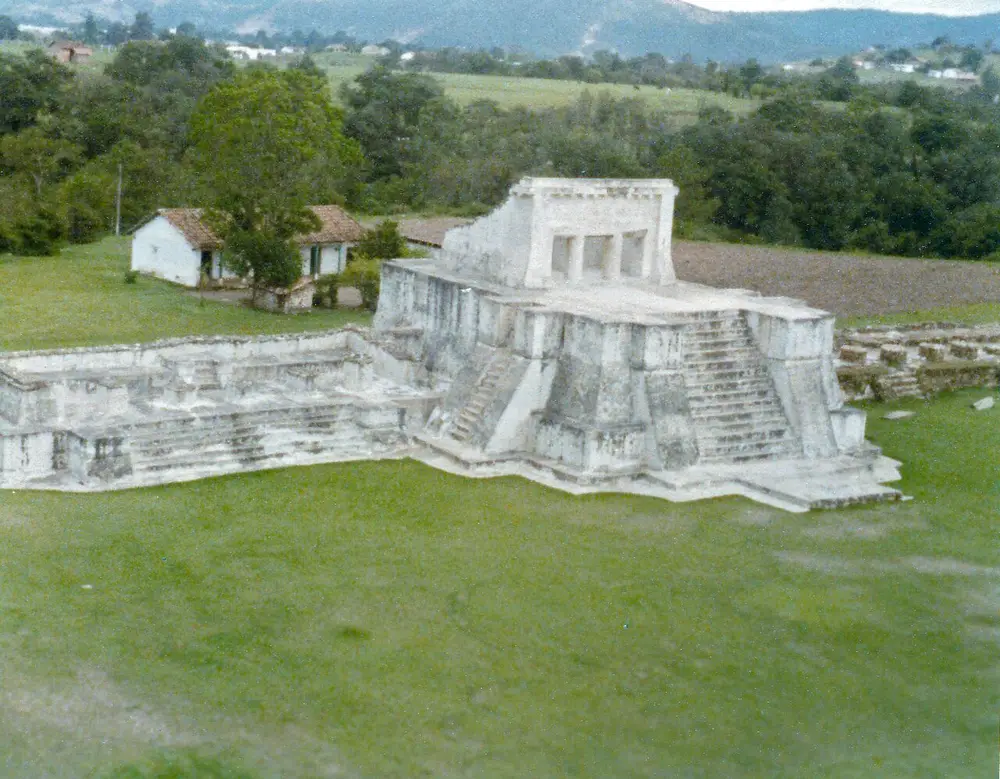 Templo piramidal restaurado de Zaculeu en 1979, con escalinatas laterales y una casa de techo rojo al fondo