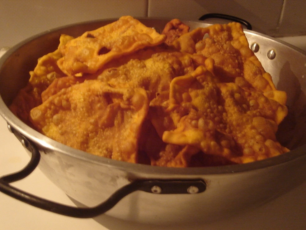 Sartén hondo lleno de hojaldras recién fritas, doradas y con ampollas en la superficie, apoyado sobre una mesa