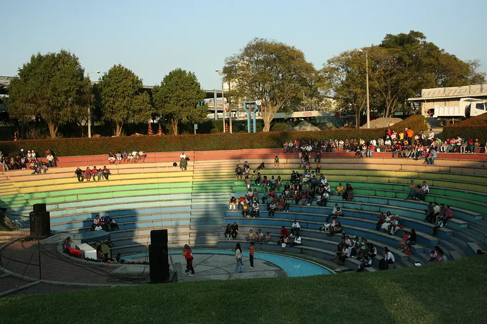 Anfiteatro de gradas de colores en un parque del IRTRA en Petapa, con personas sentadas al atardecer