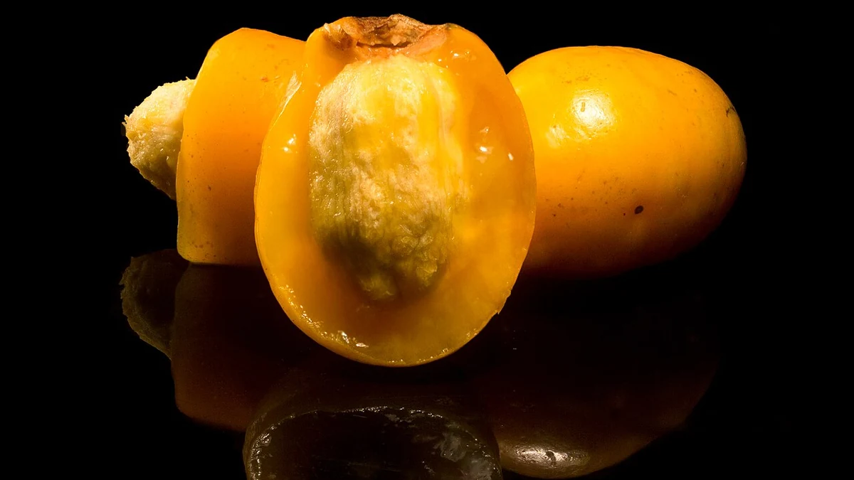 Frutos naranjas de ciruela o jocote, uno cortado con su hueso, sobre fondo negro