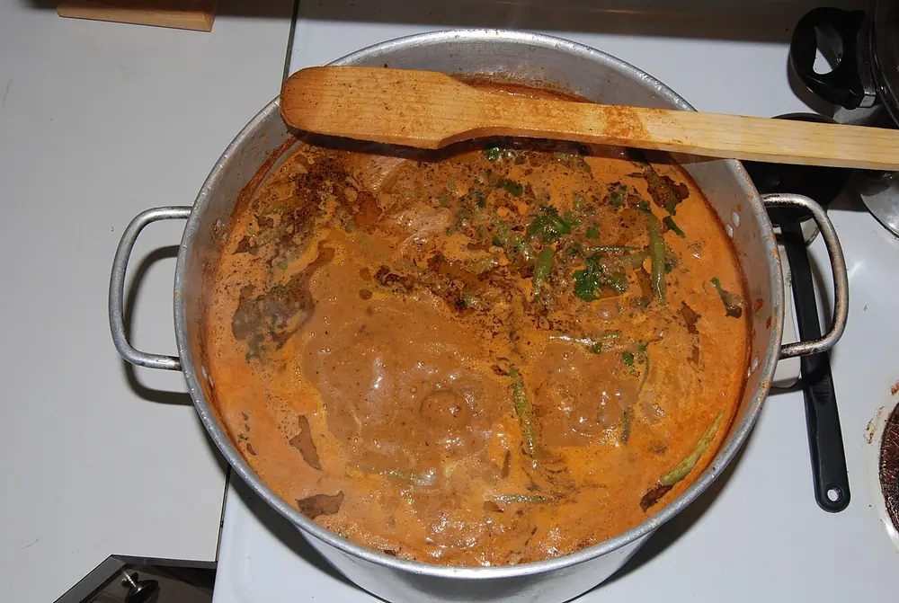 Olla de aluminio con un guiso espeso de color naranja y una cuchara de madera