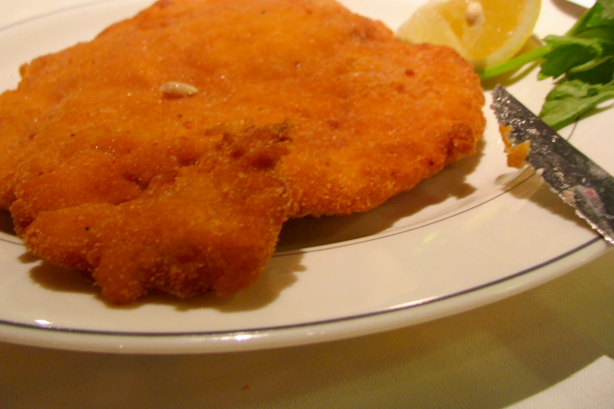 Milanesa de res empanada y frita sobre un plato blanco, con una rodaja de limón y perejil fresco al lado
