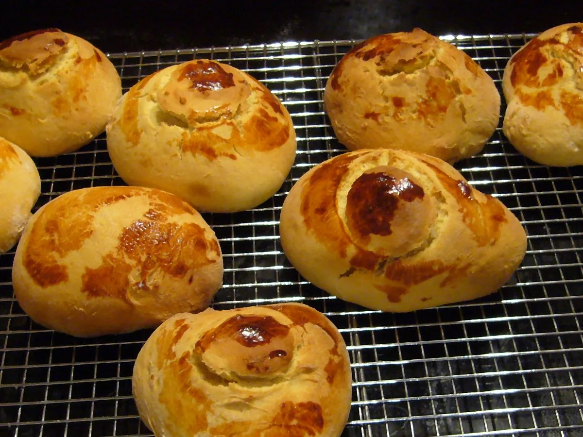 Bollos de pan de yemas guatemalteco recién horneados sobre una rejilla metálica, con la parte superior desprendida y dorada