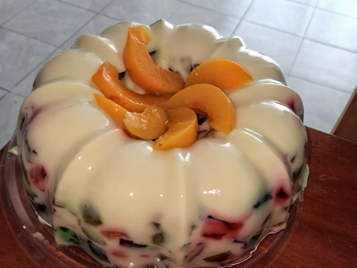 Gelatina de mosaico con crema y trozos de durazno en almíbar sobre una base de vidrio