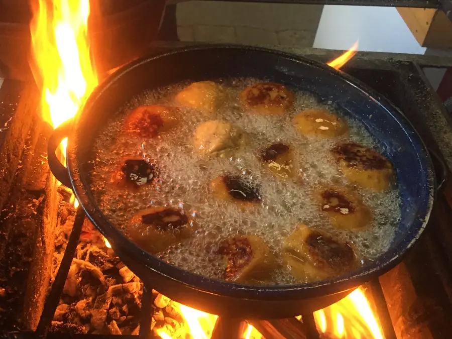 Sartén grande con rellenitos de plátano friendo en aceite sobre una hornilla de leña, con llamas alrededor