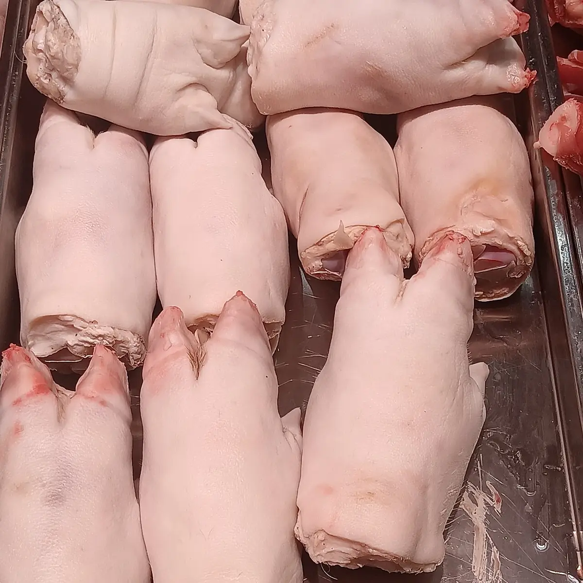 Patitas de cerdo crudas y limpias sobre una bandeja de metal