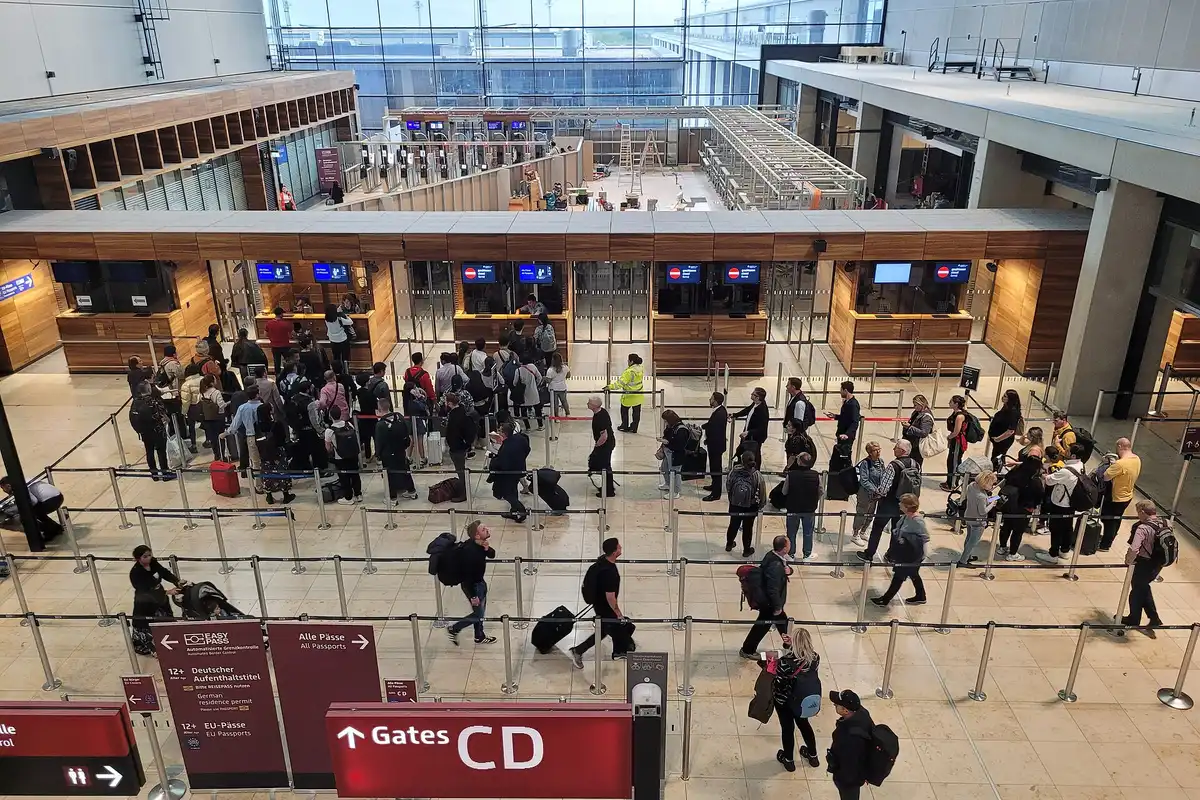 Pasajeros en fila frente a los mostradores de control de pasaportes de un aeropuerto europeo, con el rótulo All Passports a la vista