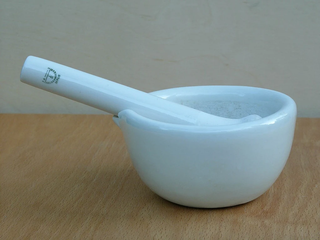 Mortero de porcelana blanco con su mano, sobre una mesa de madera