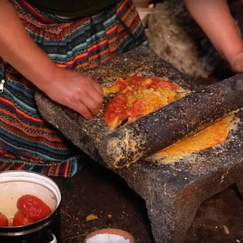 Mujer muele pepitoria y tomate en una piedra para preparar boxboles