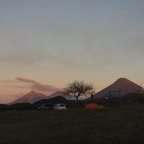 Tiendas de campaña al atardecer con volcanes al fondo en Finca El Amate