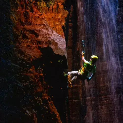 Persona haciendo rappel en una cascada iluminada de Finca El Barretal