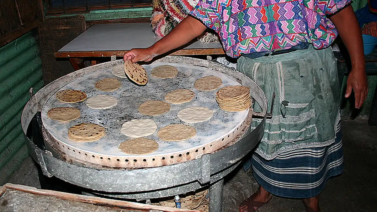 Mujer con traje típico voltea tortillas de maíz sobre un comal redondo en Guatemala