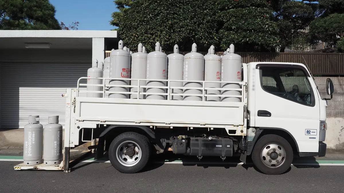 Camión blanco de reparto cargado con cilindros de gas grises estacionado en una calle