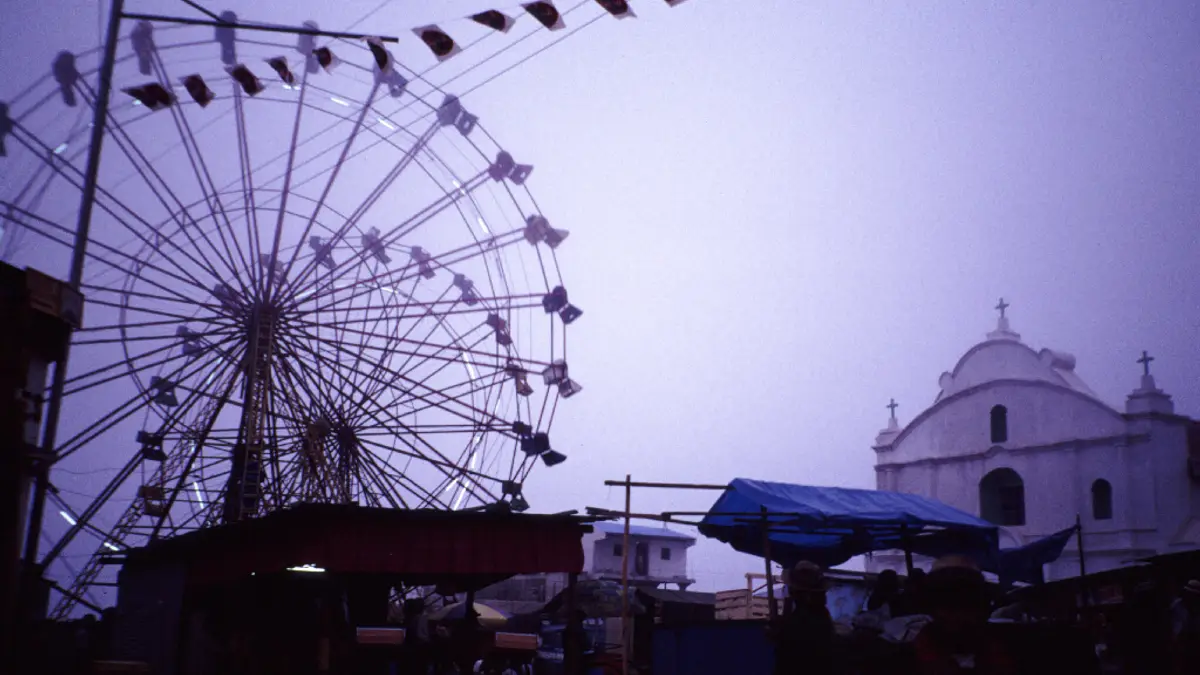 Plaza de Todos Santos Cuchumatán envuelta en neblina, con una rueda de feria y la iglesia blanca al fondo