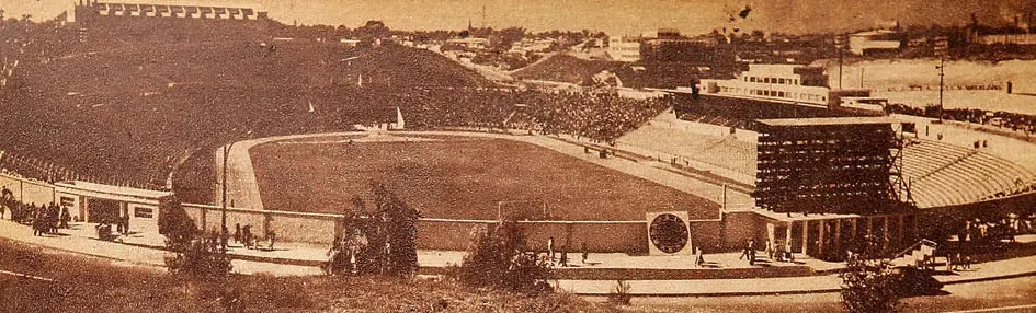 Vista panorámica en blanco y sepia de un estadio con pista de atletismo, graderías llenas y tribunas, tomada en 1950