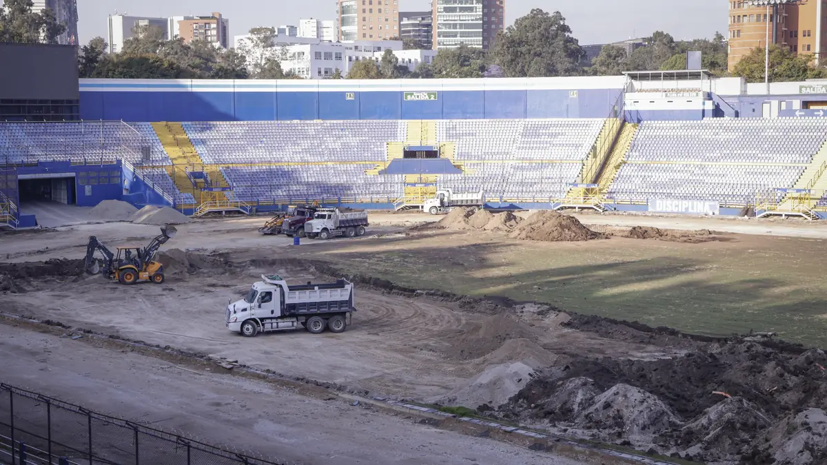 Graderías azules y vacías del Estadio Doroteo Guamuch Flores, con maquinaria y montículos de tierra sobre la cancha durante su remozamiento