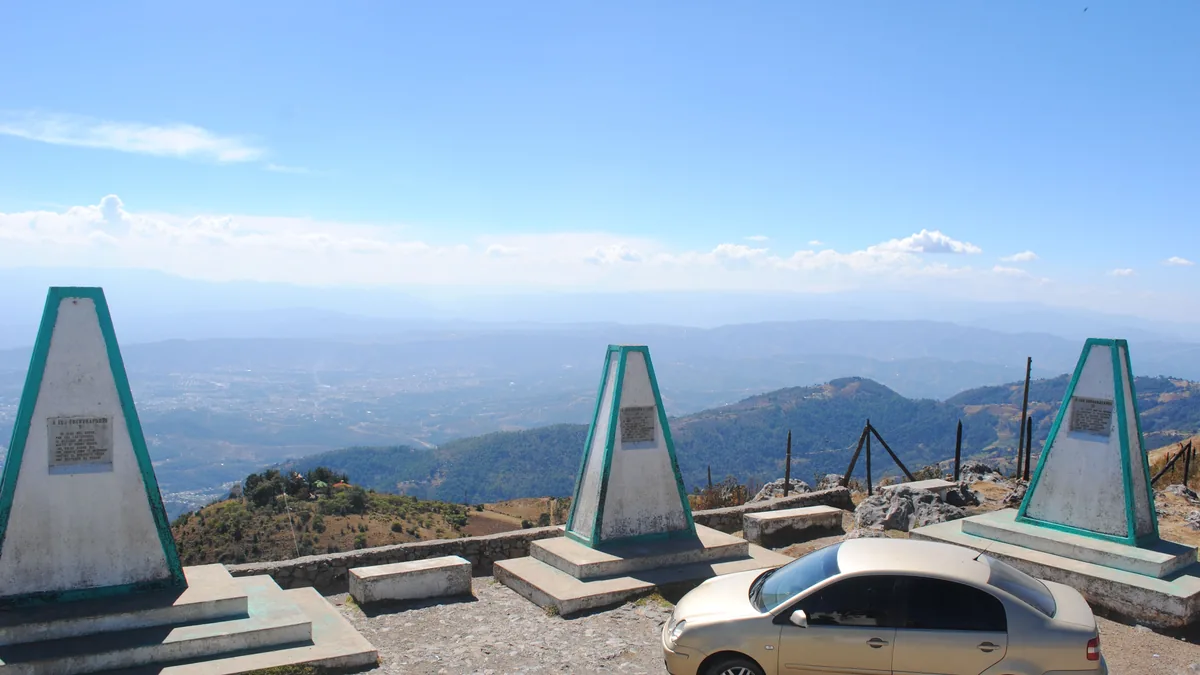 Mirador en la Sierra de los Cuchumatanes, con montañas azules, un vehículo y monumentos de piedra en primer plano