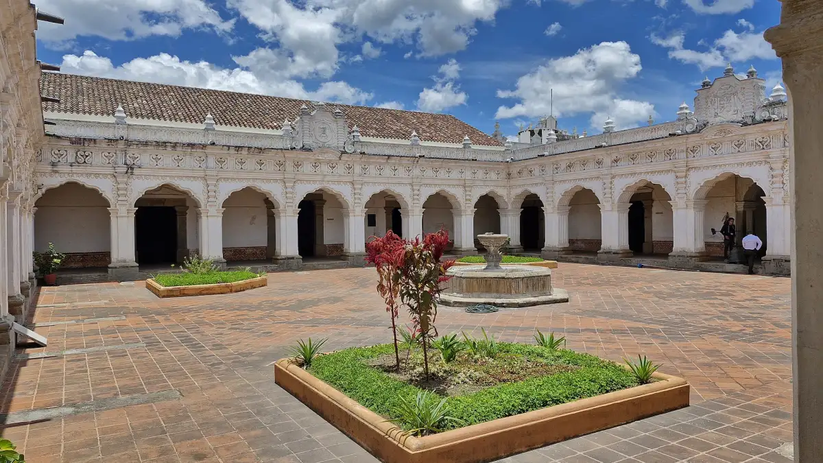 Patio interior del Museo de Arte Colonial de Antigua Guatemala, con arcos blancos, jardineras y una fuente de piedra