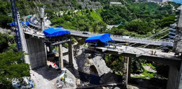Vista aérea del nuevo puente Corozal sobre un barranco, con dos carros de avance cubiertos por lonas azules y el puente actual al fondo