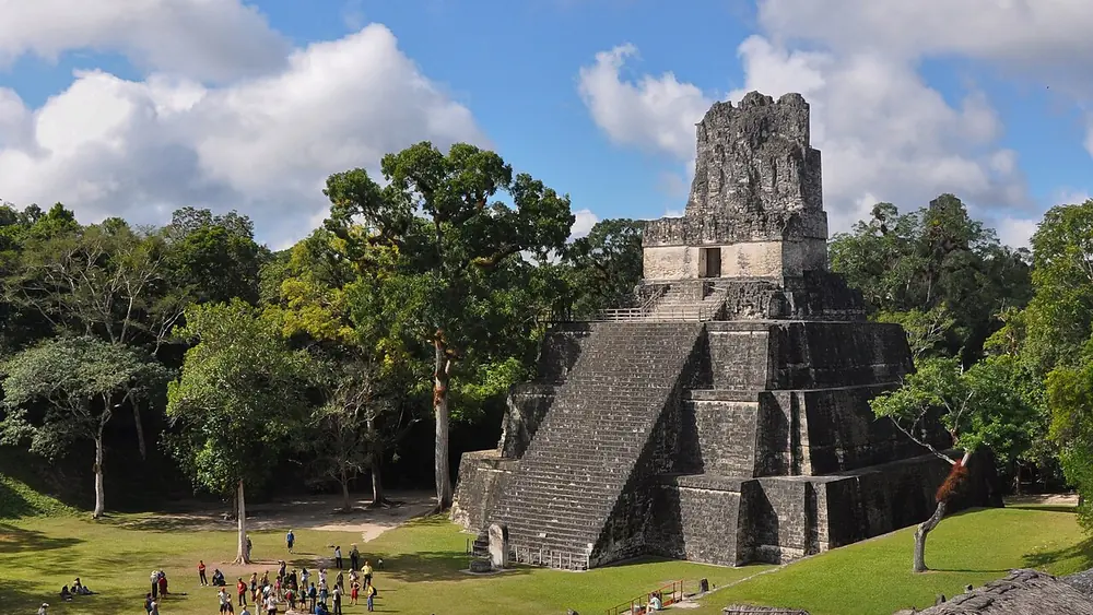 Templo II de Tikal, con una gran pirámide de piedra y árboles alrededor, bajo un cielo con nubes