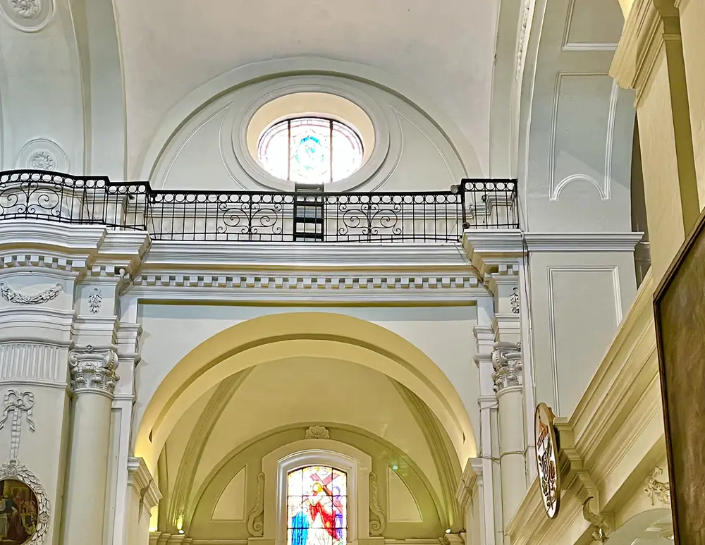 Interior de una iglesia barroca con bóveda clara, arco central, altar al fondo y una ventana con vitral de color