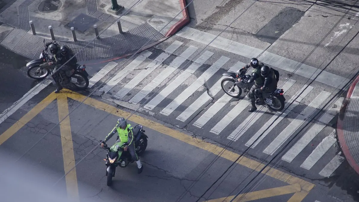 Agentes de la Policía Nacional Civil en motocicleta cruzando un paso peatonal en una calle de la Ciudad de Guatemala