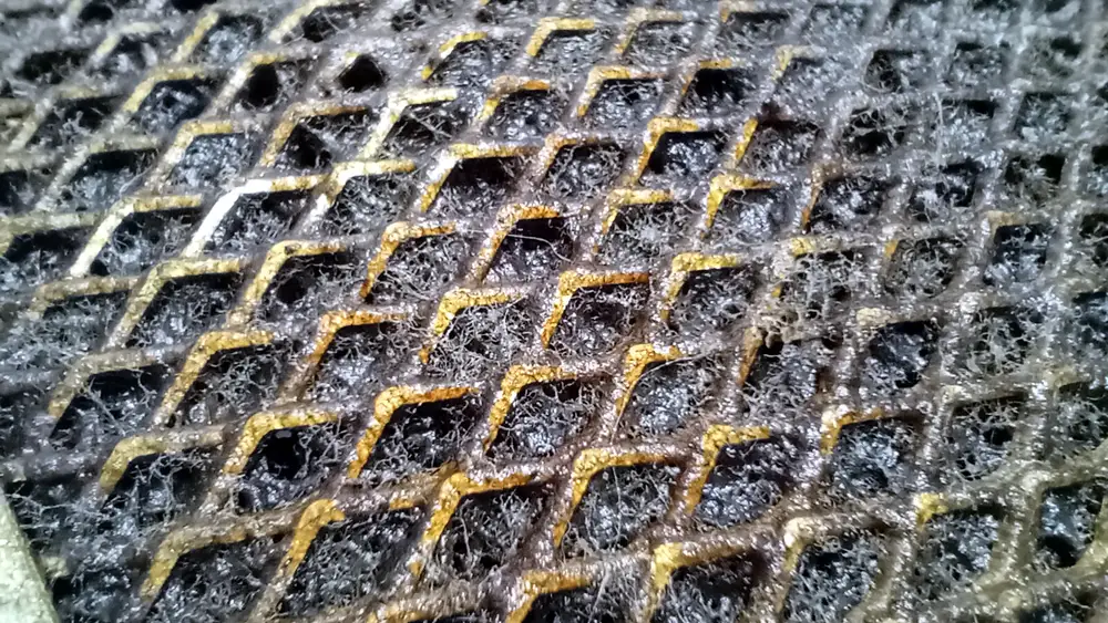 Primer plano de una malla metálica de campana de cocina cubierta por una capa espesa de grasa seca y polvo doméstico