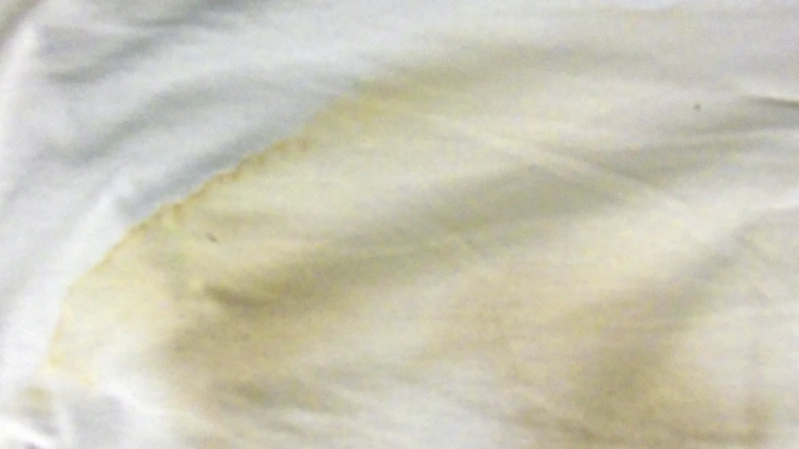 Mancha seca de color amarillo sobre la tela de una camiseta de algodón blanca