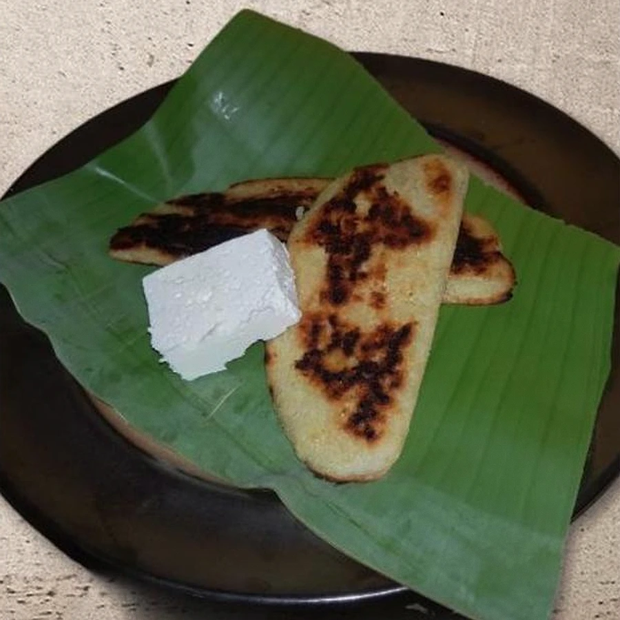 Dos riguas de elote de El Salvador doradas en el comal, servidas sobre una hoja de plátano con un trozo de queso fresco blanco
