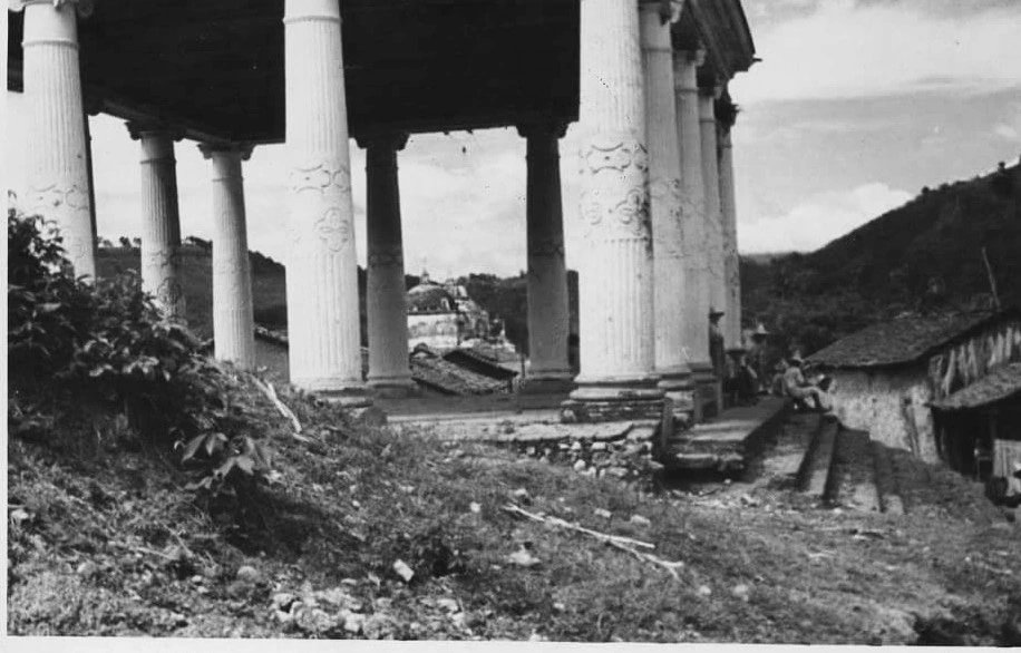 Fotografía en blanco y negro de las columnas de un templo de Minerva, con una casa de lámina a la derecha