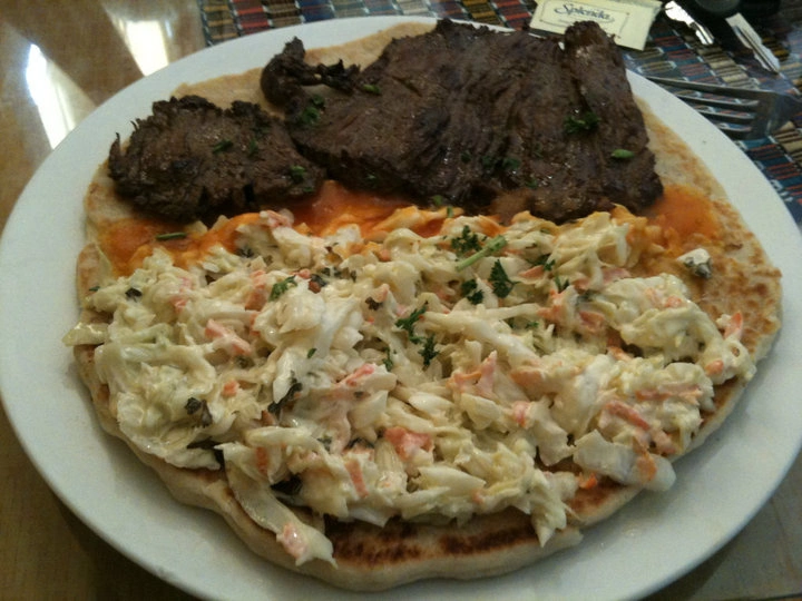 Tortilla de harina como base de un plato con ensalada de repollo, carne y frijoles, servido en Puerto Barrios