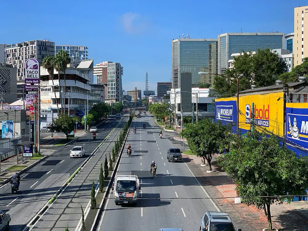 Avenida amplia con edificios de oficinas y postes de anuncios en la Ciudad de Guatemala